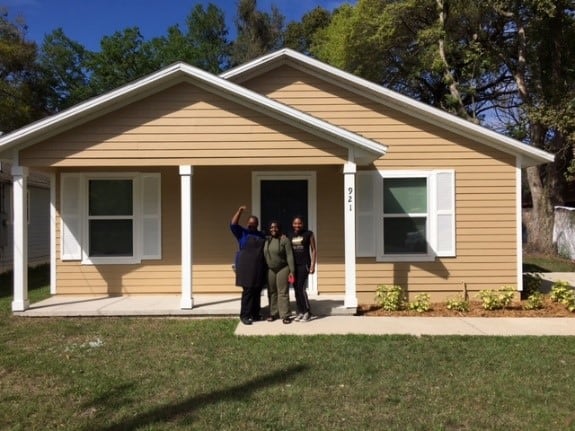 Homeowner Latoya poses in front of her brown home with two family members.