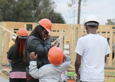 Family of four wearing hard hats watching construction of their house during Builder's Blitz
