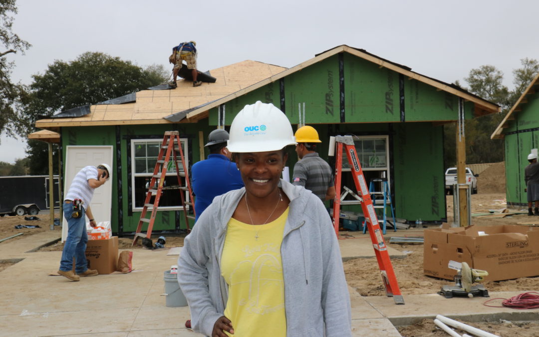 Woman wearing hard hand and smiling standing in front of in-progress home