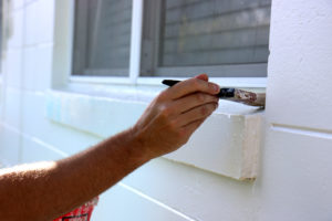 Close-up of person's hand holding a paintbrush on a white window sill
