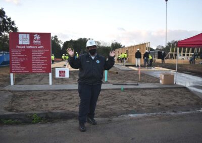 A woman waves with both hands while standing in front of dirt lot