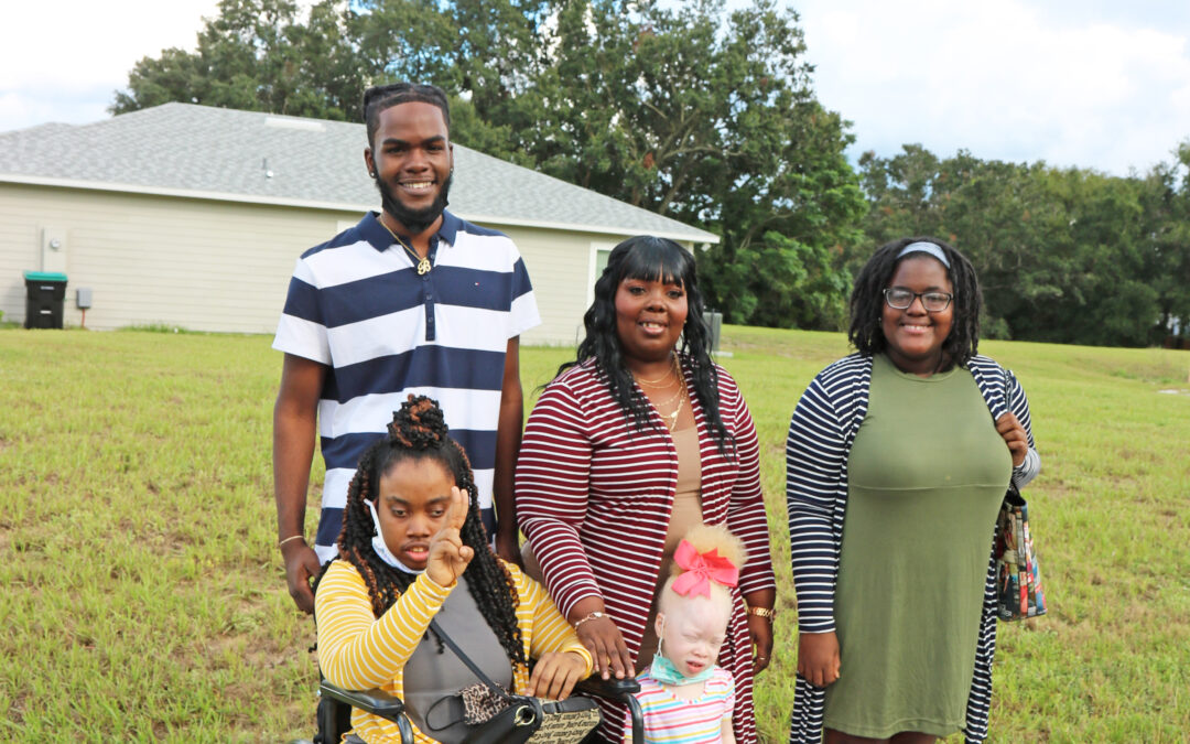 Five people smile at the camera in front of future habitat home